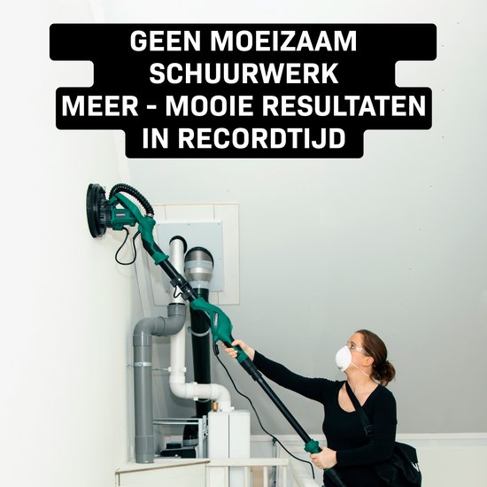 Vrouw met stofmasker gebruikt een lange groene schuurmachine op een witte muur onder een schuin dak.