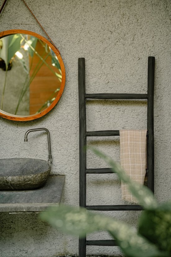 Zwarte decoratieve ladder met beige geruite handdoek, naast een wastafel met ronde spiegel.