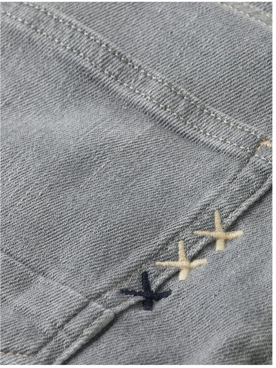 Detail van de achterkant van een grijze jeans met geborduurde 'XX' in beige en donkerblauw.
