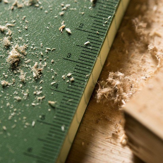 Close-up van een groene liniaal met een schaalverdeling, met zaagsel erop, op een houten ondergrond.