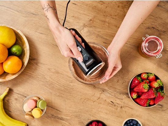 Bovenafbeelding van een vrouw die chocolademengsel mixt met een zwarte handmixer.