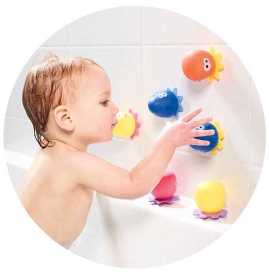Een baby speelt in bad met kleurrijk zeeleven speelgoed dat aan de muur kleeft.