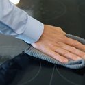 Une main avec un chiffon en microfibre gris nettoie une plaque de cuisson en verre.