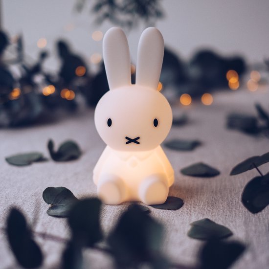 Een verlicht, wit Miffy-lampje staat op een tafel tussen bladeren en lichtjes.