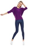 Vrouw in een paarse loszittende top met driekwart mouwen en een donkerblauwe glanzende legging, witte sneakers.