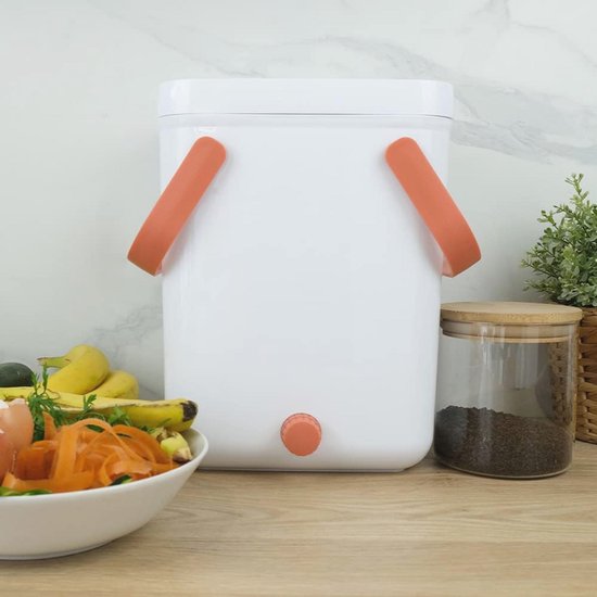 Witte keukencompostbak met oranje handvatten, met een kraantje, naast een schaal met wortel.