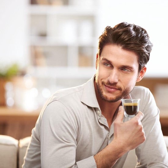 Man met een espresso in een glas, gekleed in een lichtgrijs overhemd.