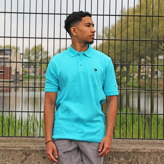 Man met turquoise polo, staand voor een hek.