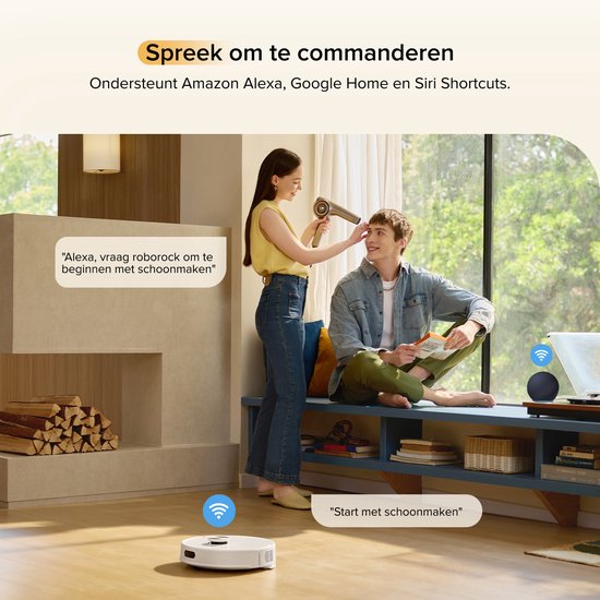 Een vrouw houdt een haardroger voor het gezicht van een man in een woonkamer. Een robotstofzuiger staat op de vloer. Spraakopdracht 'Alexa, vraag roborock om te beginnen met schoonmaken'.