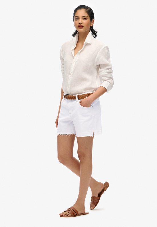 Model in wit denim short met rafelrand, witte blouse en bruine riem.