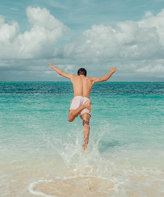 Man springt in de zee vanaf het strand, draagt een lichte paarse zwembroek.