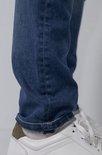 Detail van de broekspijpen van een man in een donkerblauwe spijkerbroek en witte sneakers.