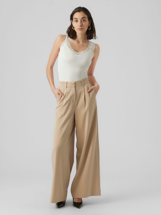 Dames model draagt een witte kanten tanktop met een beige wijde broek.