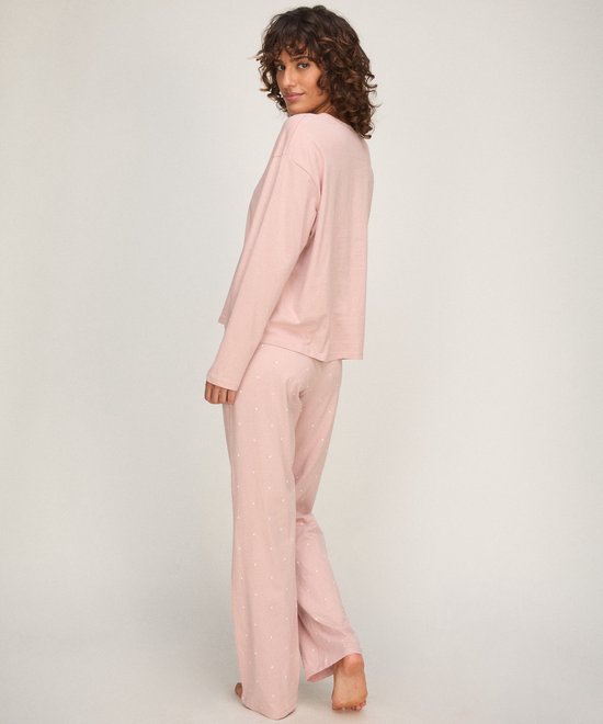Model in een zachtroze pyjamaset met lange mouwen en een all-over print van kleine witte hartjes op de broek.