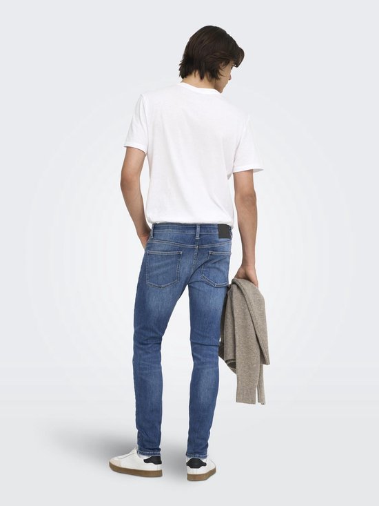 Model van achteren met een blauwe skinny jeans, wit T-shirt en beige trui.
