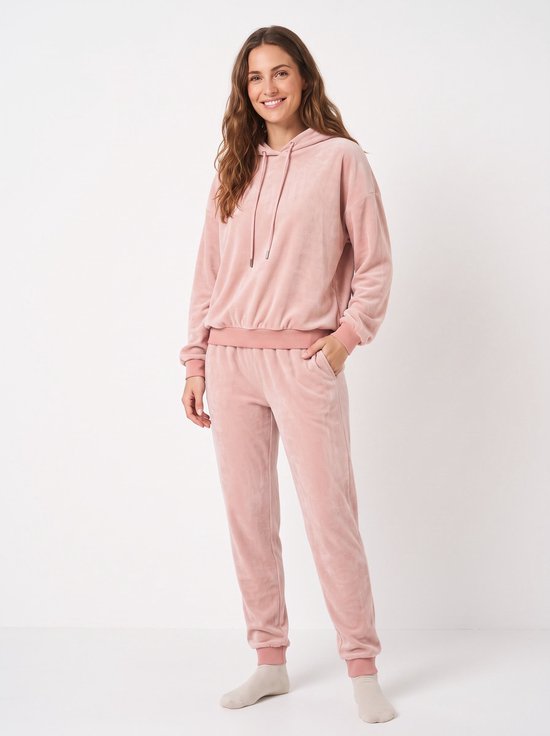 Model draagt een lichtroze fleece huispak met hoodie en bijpassende broek met boorden.