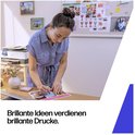 Vrouw met opgestoken haar in blauw jurkje, die aan een bureau een document beschrijft, met printer op de achtergrond.
