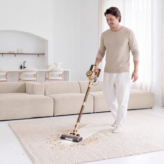 Man in beige trui en witte broek zuigt een vloerkleed met gouden en bruine steelstofzuiger.