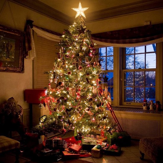 Verlichte kerstboomster als piek op een volledig versierde kerstboom in een woonkamer.