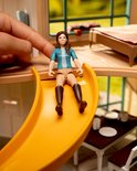 Schleich-speelfiguur met bruin haar en blauw shirt glijdt van een gele glijbaan in de Lakeside Villa.