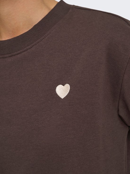 Detail van een bruine sweater met een geborduurd wit hartje op de borst.