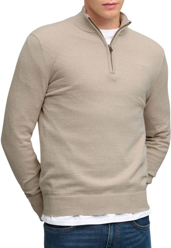 Man in beige trui met halve rits, witte t-shirt en blauwe jeans.