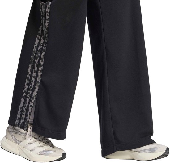 Zwarte joggingbroek met een verticale luipaardprint baan aan de zijkant, boven witte sneakers.