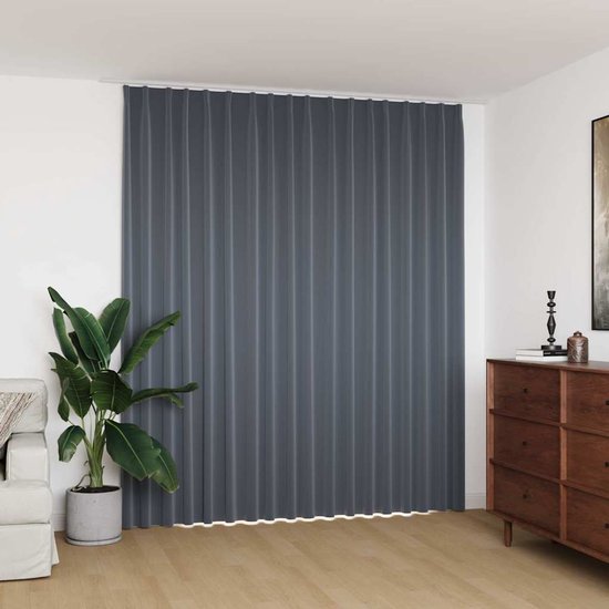 Een donkergrijs, verduisterend gordijn met plooien hangt voor een raam in een woonkamer met een bank en een dressoir.