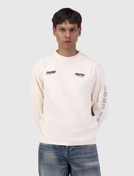 Een man met langere mouwen, ivoorkleurig t-shirt met 'PURE PATH' tekst op de borst en mouw.