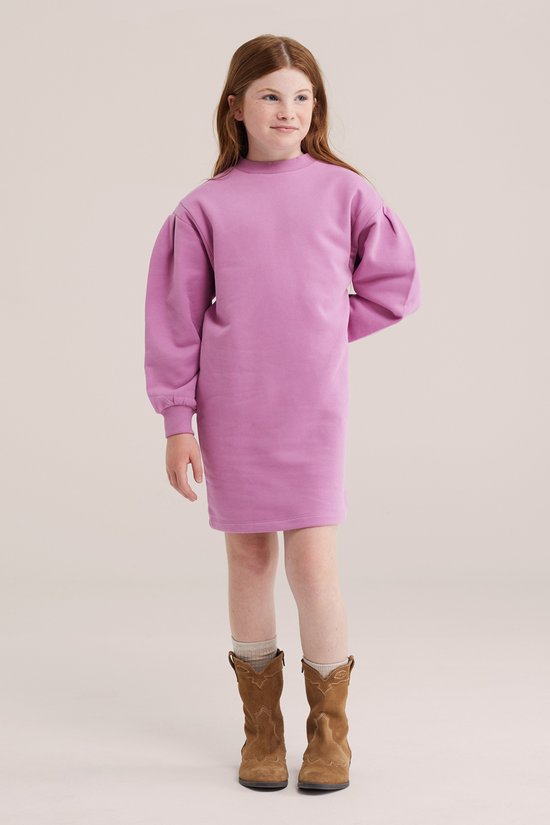Kind in een roze oversized sweatshirtjurk met pofmouwen, gecombineerd met bruine cowboylaarzen.
