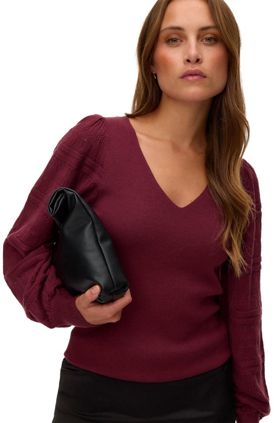 Model met bordeauxrode trui met pofmouwen met kantpatroon en zwarte clutch.