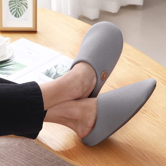 Persoon die comfortabele grijze pantoffels met wafeltextuur draagt, zittend aan een houten tafel.