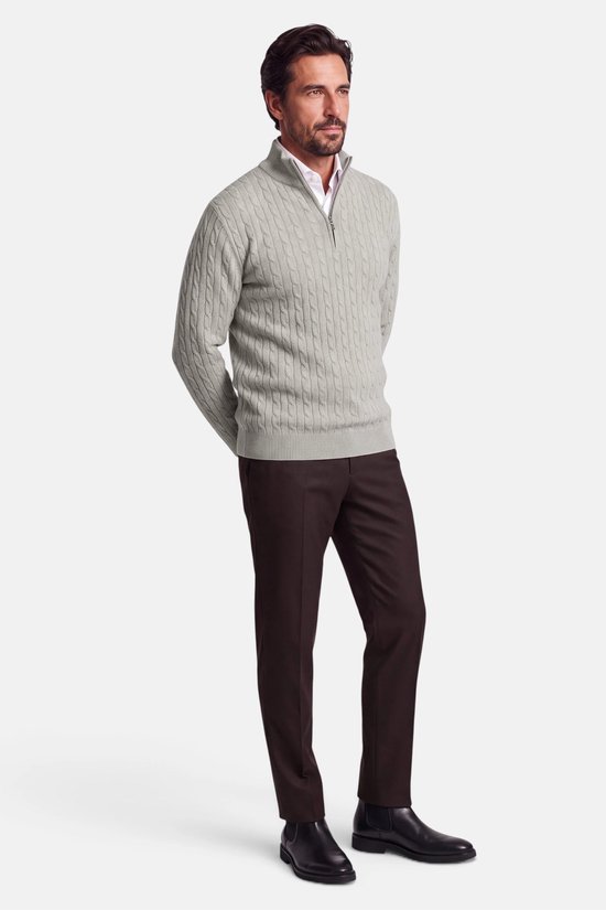 Model in grijze kabeltrui met halve rits en donkerbruine broek, staand met handen achter de rug.
