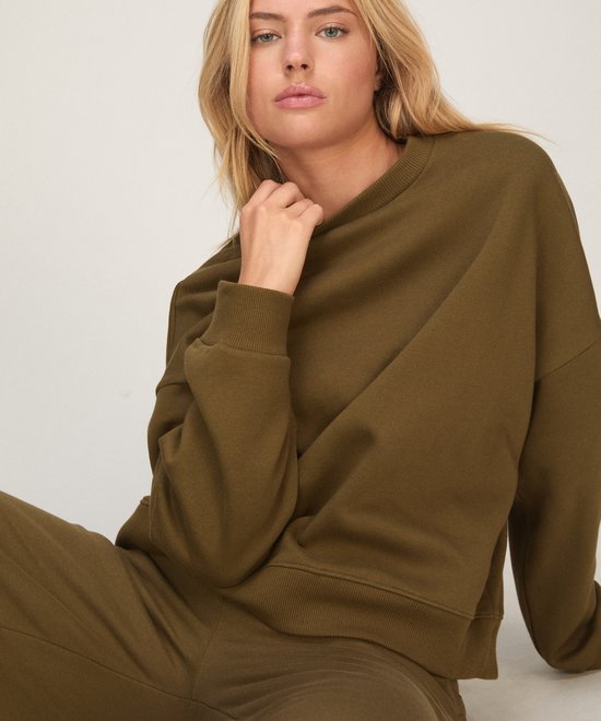 Zittend model in olijfgroene sweatshirt met ronde hals en bijpassende broek.