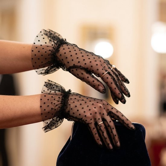 Zwarte, doorzichtige tule handschoenen met stippen en geplooide randen bij de polsen, in een elegante pose.