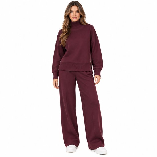 Model in een bordeaux 2-delige set met oversized coltrui met rits aan de zijkant en een wijde pantalon.