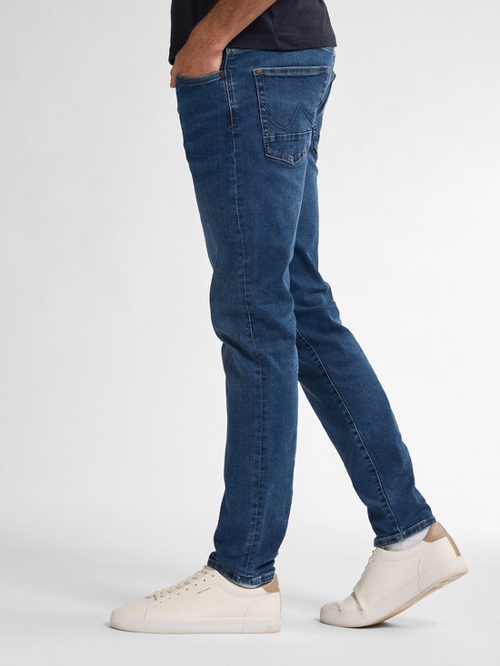 Zij-aanzicht van een man die een blauwe slim fit spijkerbroek draagt met witte sneakers.