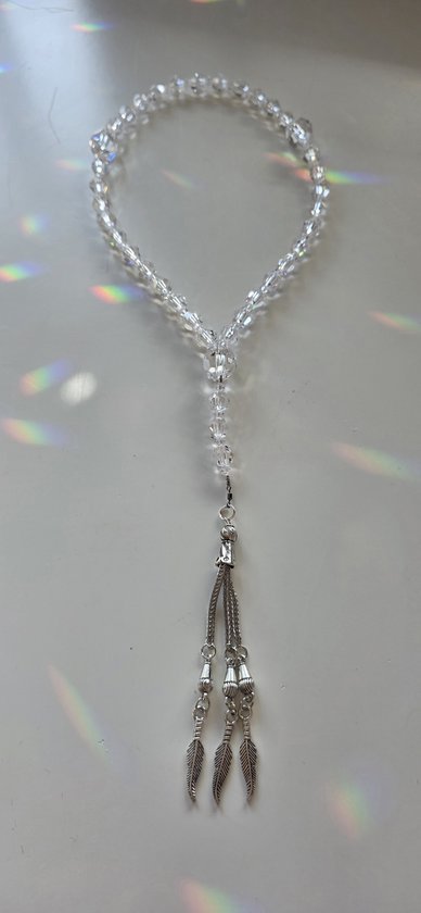 Transparante kristallen gebedsketting met zilveren kwastje en veerhangers, sfeervol verlicht.