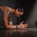 Femme en tenue de sport en position de planche sur un tapis, portant un tracker d'activité blanc au poignet.