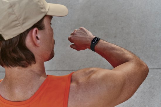 Man met beige pet en oranje sporthemd kijkt naar de zwarte Fitbit Edge om zijn pols.