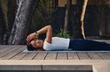 Vrouw in sportkleding ligt in meditatiehouding op een yogamat, met Fitbit Edge om de pols.