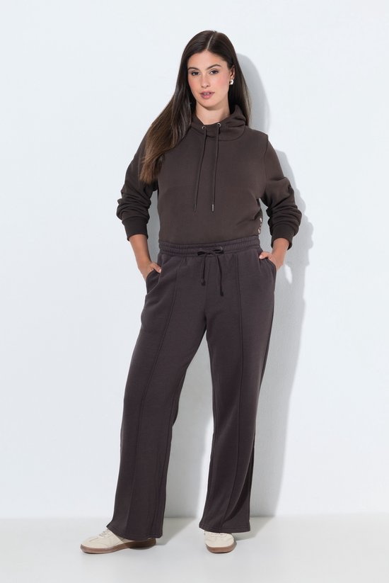 Model draagt een donkerbruine joggingbroek met wijde pijpen en bijpassende hoodie.