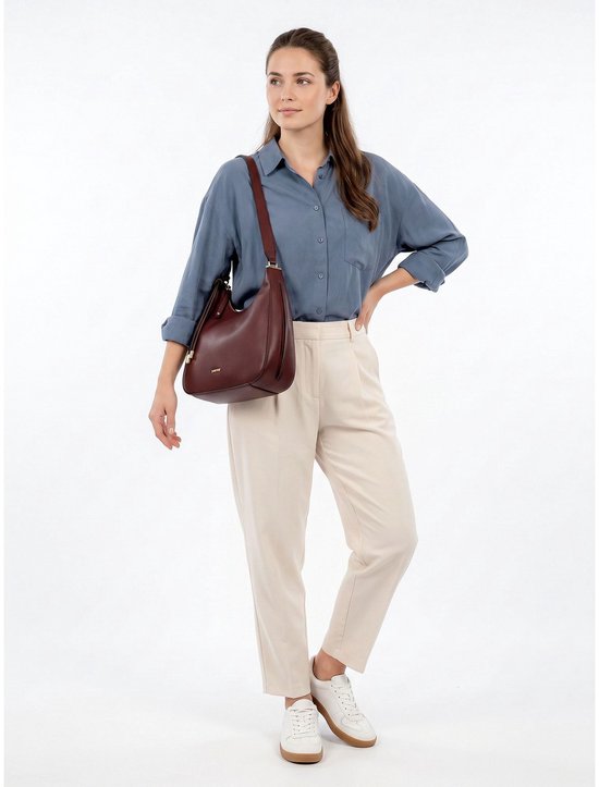 Vrouw met een bordeauxrode Suuri Frey handtas over haar schouder, gekleed in een blauwe blouse en beige broek.