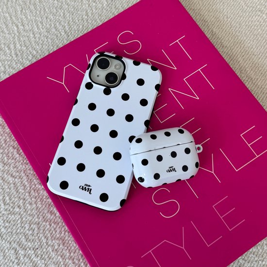 Witte telefoonhoes en witte oplaadcase met zwart stippatroon op roze boek.