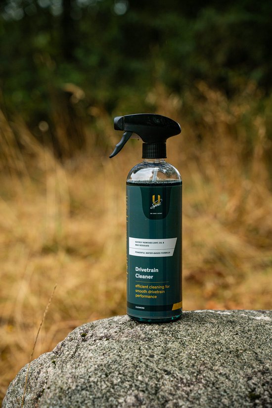 Een spuitfles U-Sport Drivetrain Cleaner met een groen label, met de tekst 'Drivetrain Cleaner', staat op een rots.