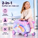 Kind zit op een eenhoorn-reiskoffer met wielen in een vertrekhal.