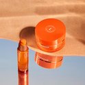 Lancaster Golden Tan Maximizer serum en balsem op spiegelend oppervlak met zand.