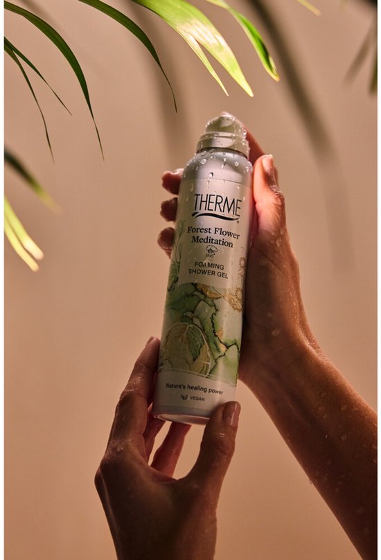 Handen houden een Therme Forest Flower Meditation Douchegel in een witte spuitbus, met waterdruppels.