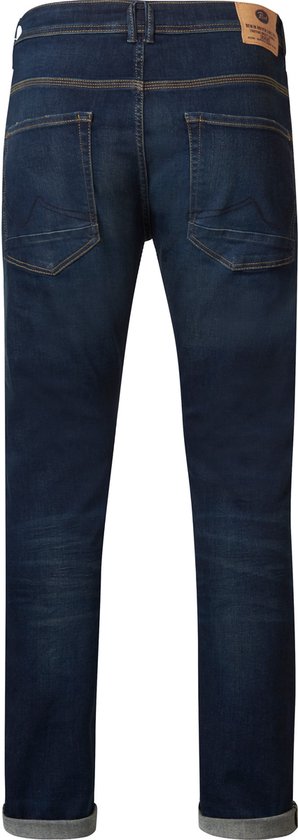 Achterkant donkerblauwe spijkerbroek met stonewash, gele stiksels en label met 'DENIM DRIVEN SINCE 1989'.