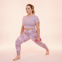 Vrouw in roze tie-dye legging en lila top, die een lunge-oefening doet met roze dumbbells.
